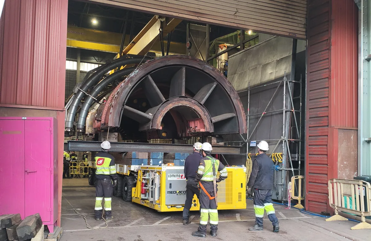 Montadores con ropa de alta visibilidad y casco preparando el traslado de una carcasa de turbina en el taller